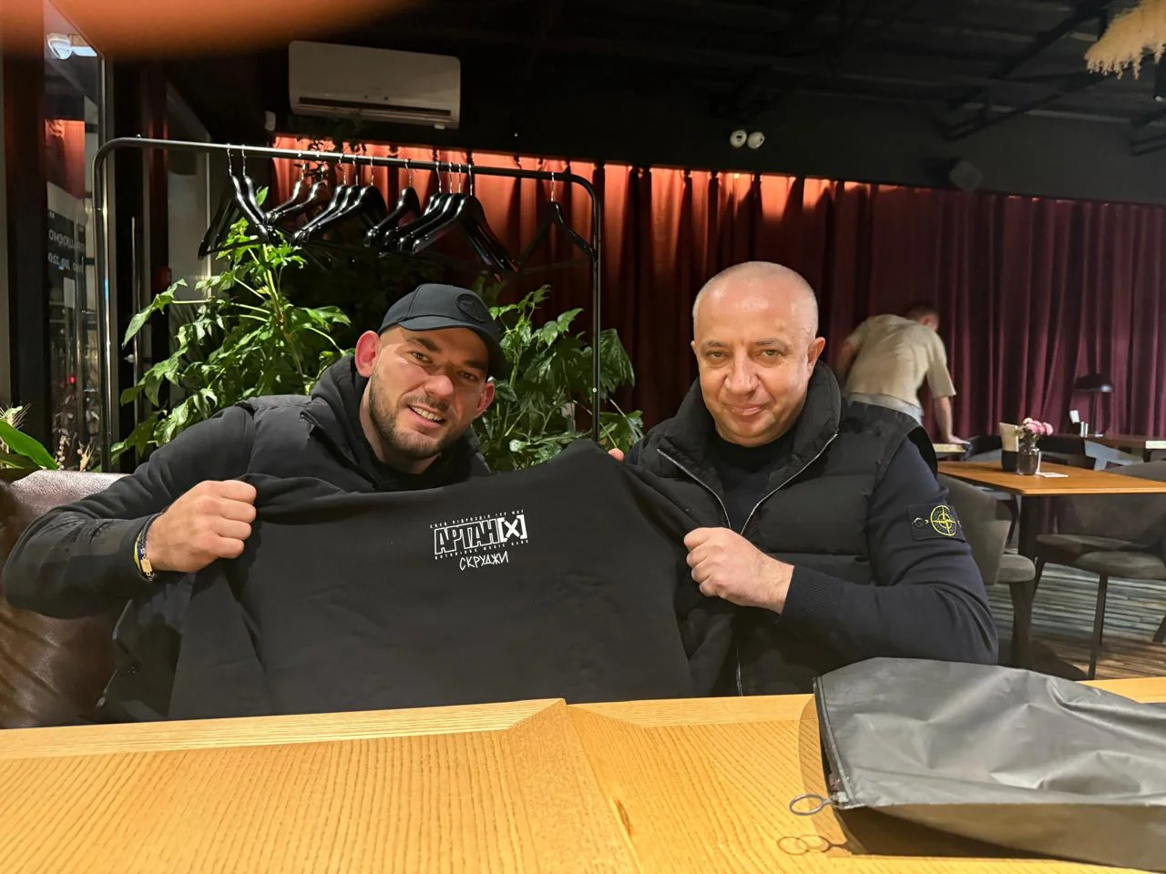 Двоє чоловіків тримають футболку Partizan City Hall у кафе
