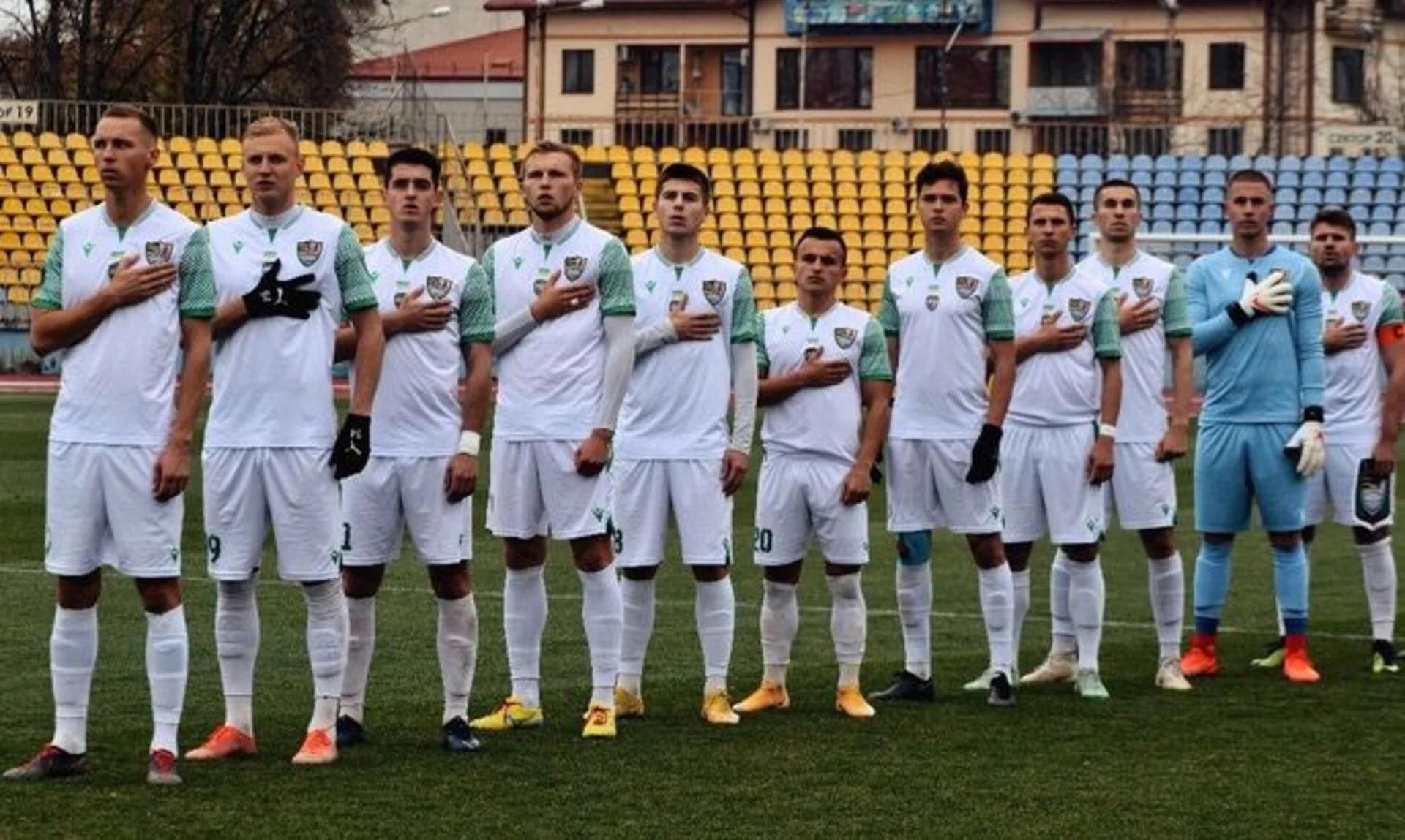 Гравці ФК «Ужгород» стоять на полі з руками на грудях під час гімну