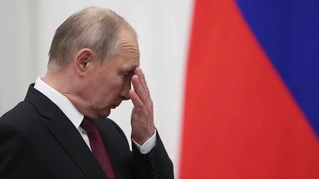 Володимир Путін з рукою на чолі на тлі прапора Росії